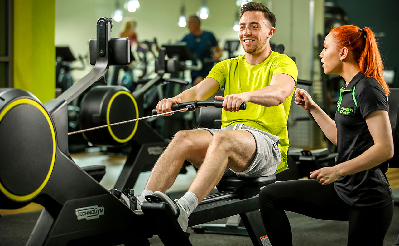 Gym member on rowing machine being instructed by personal trainer