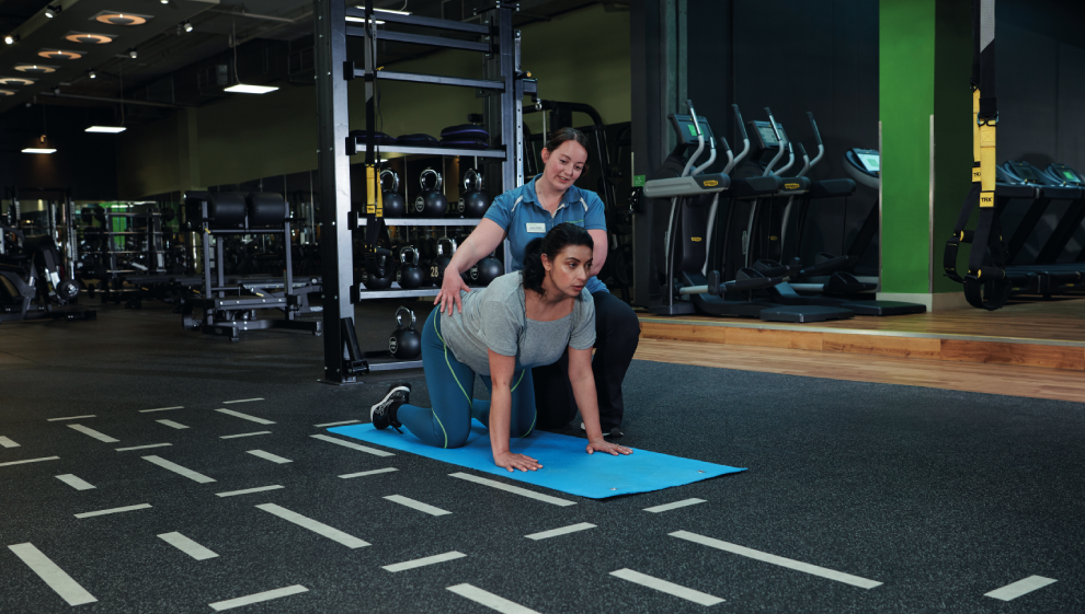 A woman performs Postnatal exercises with her Personal Trainer in a Nuffield Health Gym. 