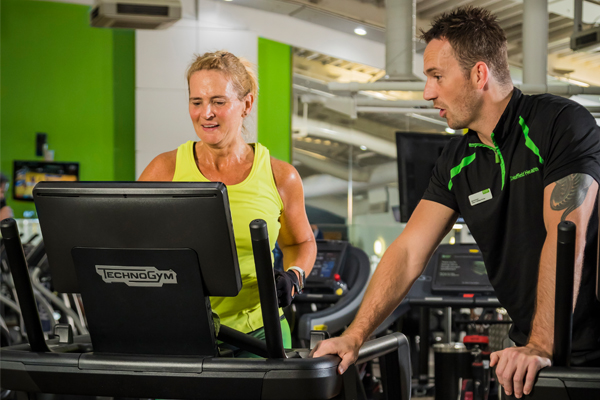 Woman in yellow top running on treadmill whilst male personal trainer is instructing her