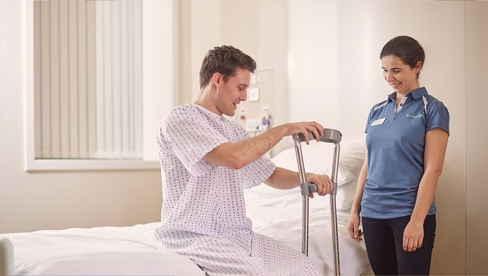 Physiotherapist helping man to get out of bed using crutches