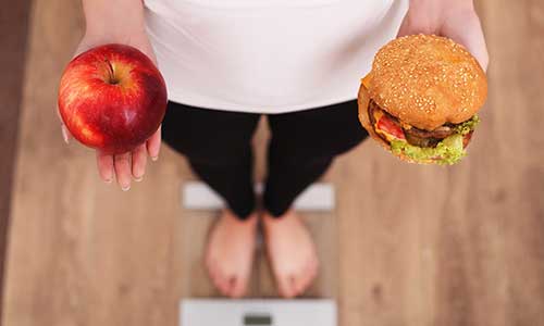 Woman deciding between apple and a burger