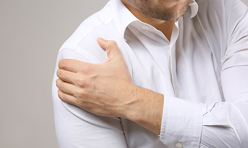 Man in white shirt clutches his shoulder in pain. close up