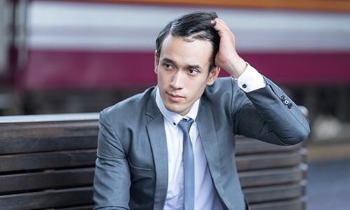 Businessman in a grey suit sitting on a bench looks like he's having a crisis of confidence