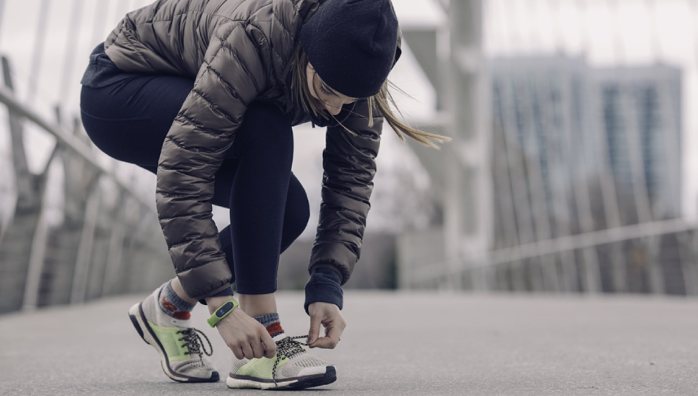 A woman on a run during winter fixes her shoelace