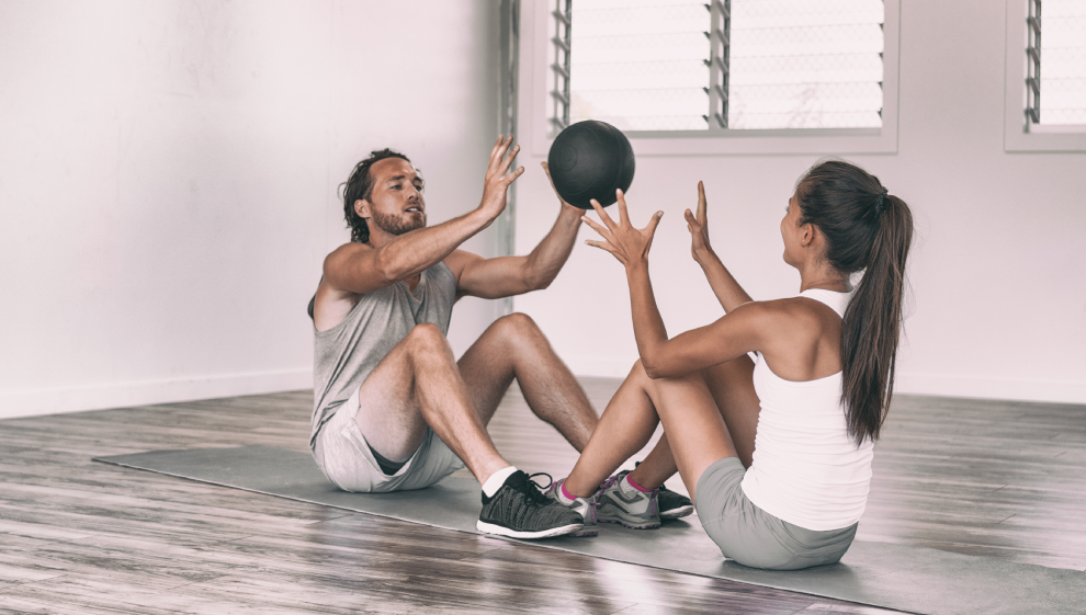 a couple performing a sit-up to medicine ball throw