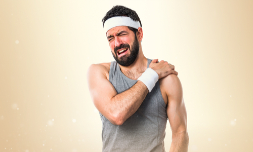 Man in sportswear holding his shoulder in animated pain