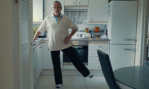 Man performing side leg raises while standing in kitchen