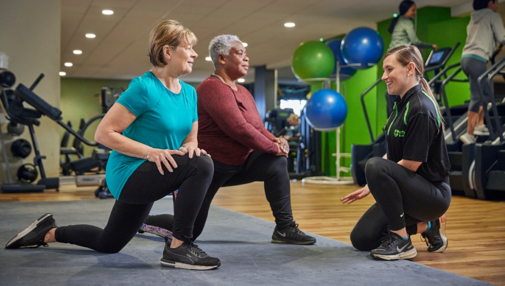 Two elderly gymgoers stretching with their PT