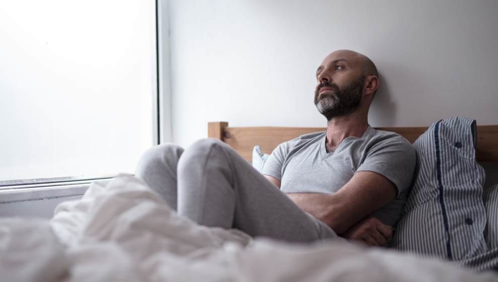 A man laying in bed struggles to sleep due to mental health issues